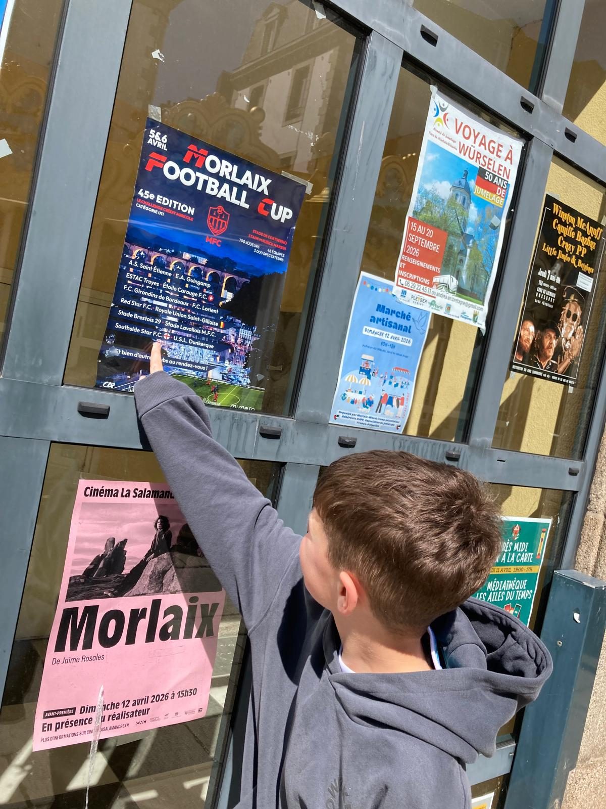 A Cheetahs player pointing up at the Morlaix Football Cup poster in the town