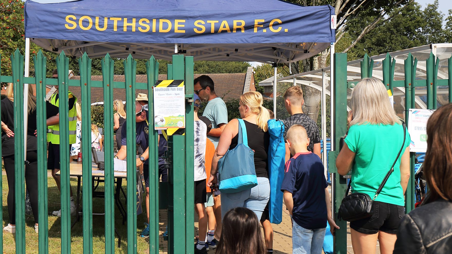 Families queuing at the branded Southside Star F.C. gazebo on the gate at a club fun day
